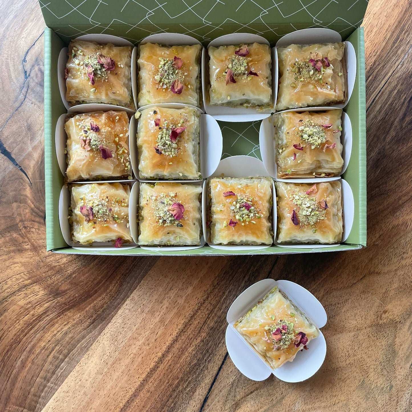 Box of square baklawa  with a single baklawa in its casing on a wooden surface